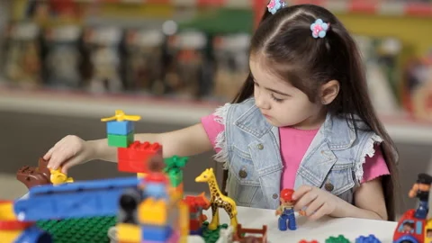 Cute little girl is playing with objects made of plastic elements, blocks of Stock Footage 87960252