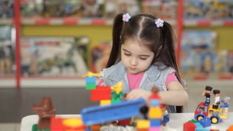 Cute little girl is playing with objects made of plastic elements, blocks of Stock Footage 87960365
