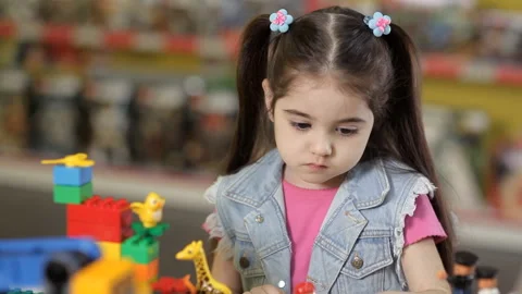 Cute little girl is playing with objects made of plastic elements, blocks of Stock Footage 87960446