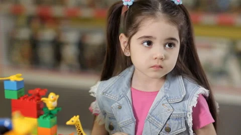 Cute little girl is playing with objects made of plastic elements, blocks of Stock Footage 87960530