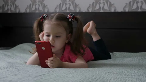 A cute little girl is playing with a smartphone, watching a video in the phone Stock Footage