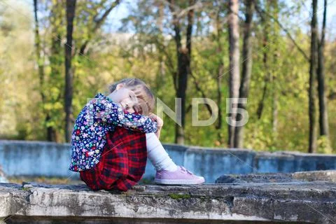 Cute little girl in red skirt sits on old fountain in sunny green park Stock Photos