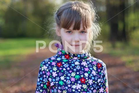 Cute little girl stands in sunny green park, shallow dof, close up Stock Photos