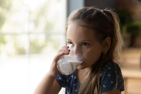 Cute little kid girl drinking glass of fresh yoghurt. Stock Photos