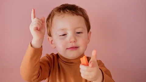 Cute little red-haired boy eats a carrot on a pink background Stock Footage 127702407