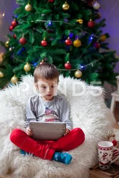 Cute little sick boy, sitting on bean bag, playing on tablet Stock Photos