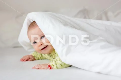 Cute little six month old baby boy, playing under duvet at home in bed in bed Stock Photos