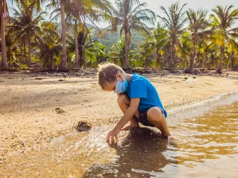 Cute little young blond boy with medical face mask on the beach playing with Stock Photos