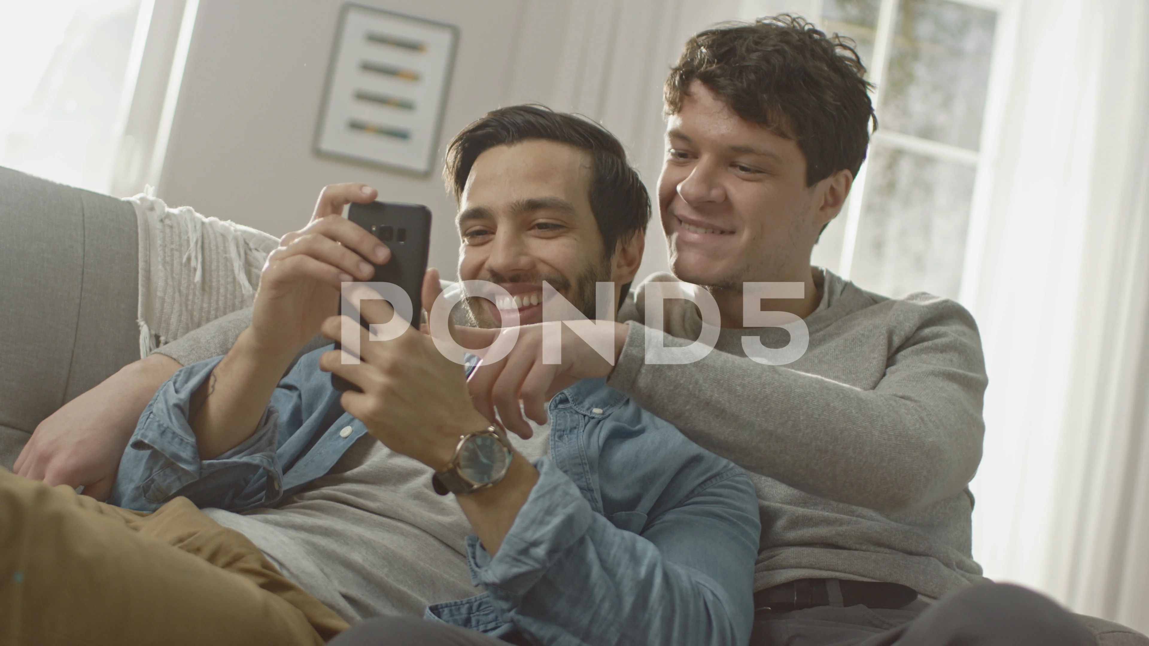 Cute Male Gay Couple Spend Time at Home. They are Lying Down on a Sofa and  Use