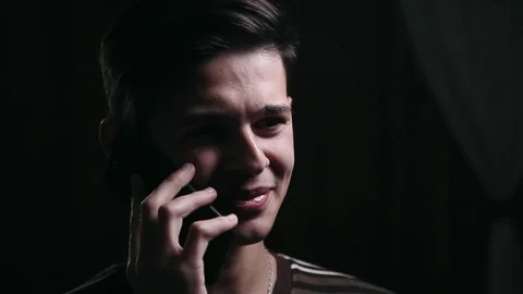 Cute man talking on the phone in the dark room, close up Stock Footage 99050752