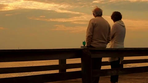 Cute old couple watching the sunset together over the dock Stock Footage