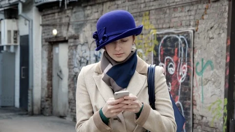 Cute person in hat closeup texting message phone with serious face on street 4K. Stock Footage 119515810