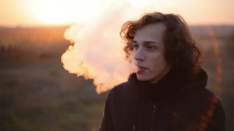 Cute portrait of vaping guy in the field at sunset.Closeup Видео 98749675