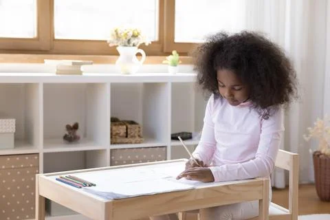 Cute preschool African girl drawing seated at table in nursery Stock Photos