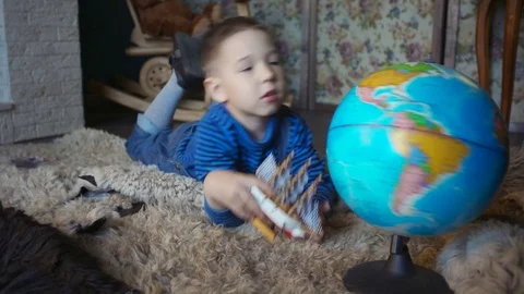 Cute preschool boy rotating globe lying on floor in children's room Stock Footage 76149392