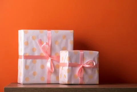 Cute present boxes on wooden table against orange wall. Stock Photos