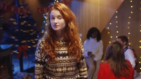 Cute pretty red-haired young woman wearing Christmas sweater staying with Stock Footage 121593296