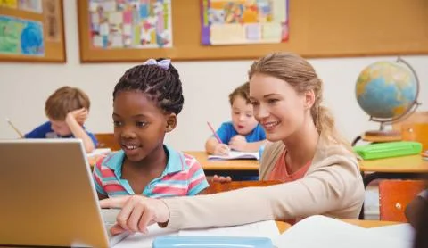 Cute pupil using computer with teacher Stock Photos