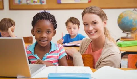 Cute pupil using computer with teacher Stock Photos