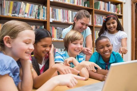 Cute pupils using tablet computer in library Stock Photos