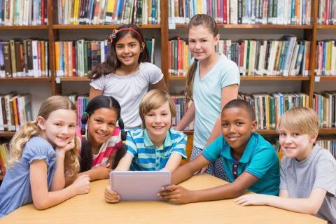 Cute pupils using tablet computer in library Stock Photos