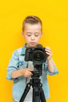Cute puzzled kid adjusts the camera on tripod Stock Photos