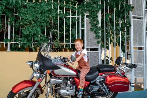 Cute red-haired boy sits on a big motorcycle, summer vacation and fun Stock Photos