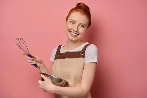 Cute red-haired girl with a high bun in a beige apron and a face in flour Stock Photos