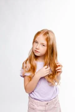 Cute red-haired long-haired girl in daily clothes (skirt, T-shirt) braids her Stock Photos