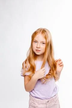 Cute red-haired long-haired girl in daily clothes (skirt, T-shirt) braids her Stock Photos