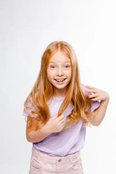 Cute red-haired long-haired girl in daily clothes (skirt, T-shirt) braids her Stock Photos