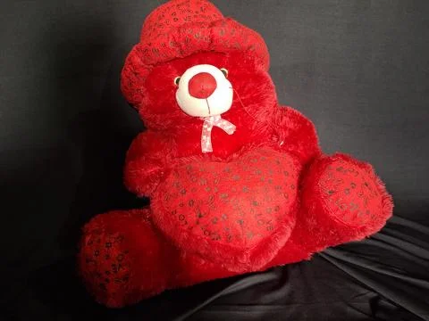 A cute red teddy bear sits against a soft Stock Photos