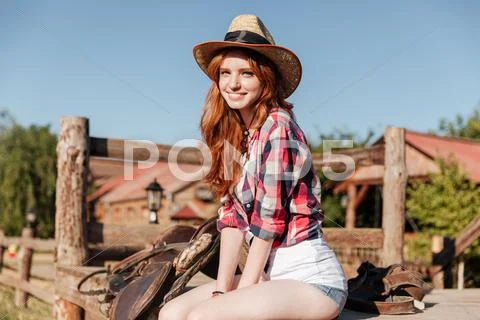 Cute redhead cowgirl sitting and resting on the ranch fence Stock Photos