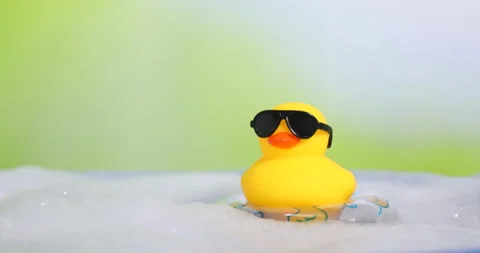 Cute rubber duck floating in water with bubbles against blurred green Stock Footage 309858307