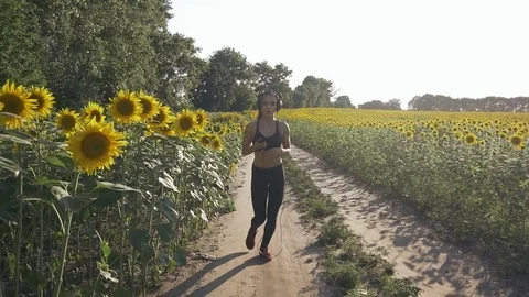 Cute runner girl runs across the field. She listens to music on headphones. Stock Footage