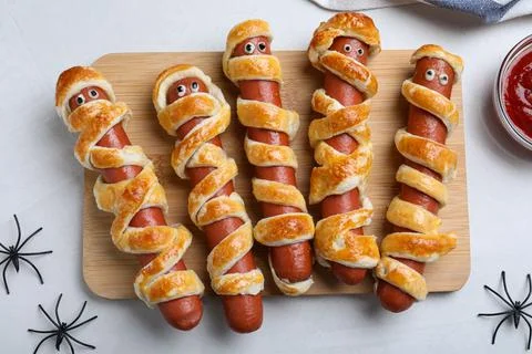 Cute sausage mummies served on white table, flat lay. Halloween party food Stock Photos