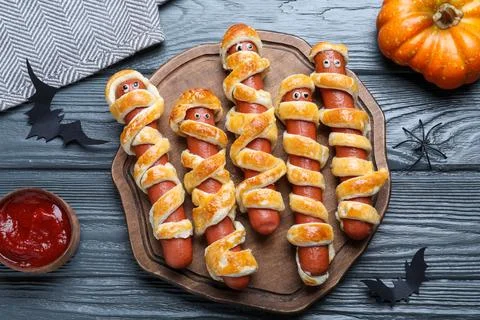 Cute sausage mummies served on wooden table, flat lay. Halloween party food Stock Photos