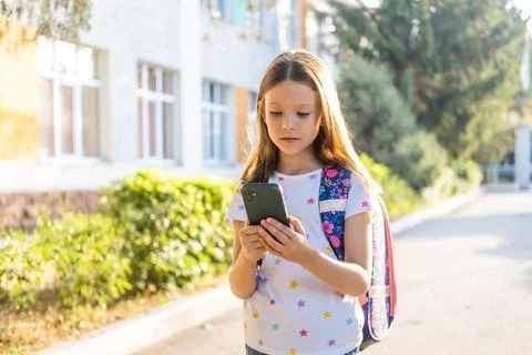 Cute school girl with backpack using smartphone Stock Photos