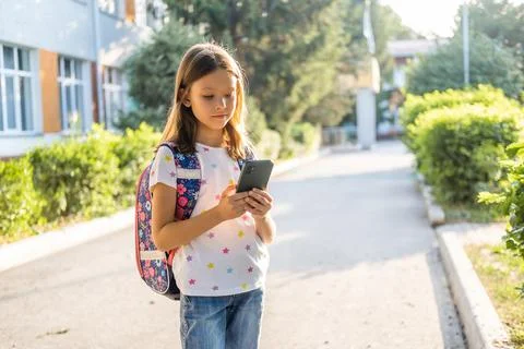Cute school girl with backpack using smartphone Stock Photos