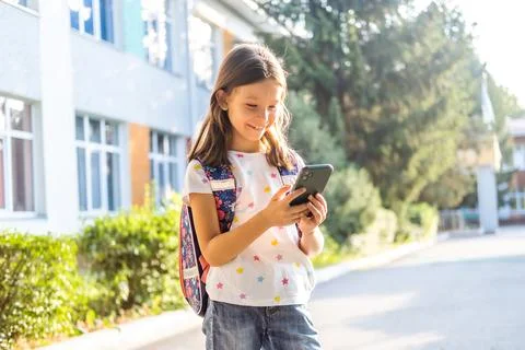 Cute school girl with backpack using smartphone Stock Photos