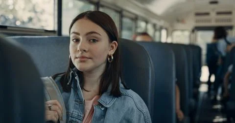 Cute school girl posing in schoolbus close up. Brunette schoolgirl sitting bus. Stockfoto's