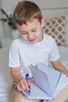 Cute schoolboy doing homework on the bed. A little boy of 7 years old is doin Foto stock