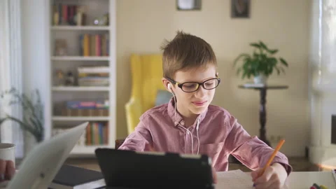 Cute schoolboy is doing homework at table with tablet during quarantine at home Stock Footage 131080533
