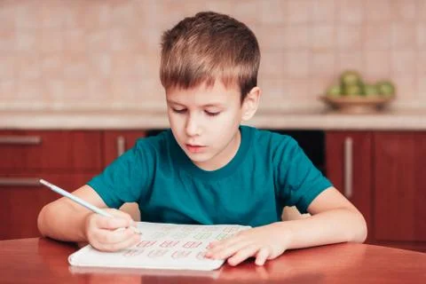 Cute schoolboy learn math at homework sitting by table in kitchen Stock Photos
