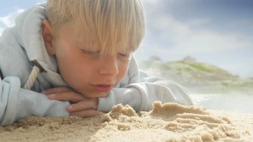 Cute Schoolboy lying with head on hands at the beach looking at sand Video stock 85609449