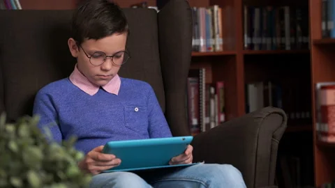 Cute schoolboy uses the app on his smartphone while sitting in a chair Stock Footage 96550452