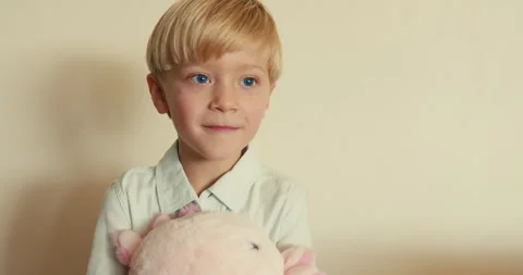 Cute shot of a blond boy gently hugging his favorite soft toy and happily 스톡 동영상 346982854