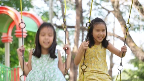 Cute sisters are having fun playing on the swings in a playground in a park. Stock Footage 291791889