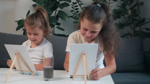 Cute sisters writing or working on paper in kindergarten with paintbrush Stock Footage 282659280