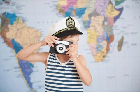 Cute small boy in captain hat taking picture with retro film camera map backd 스톡 사진